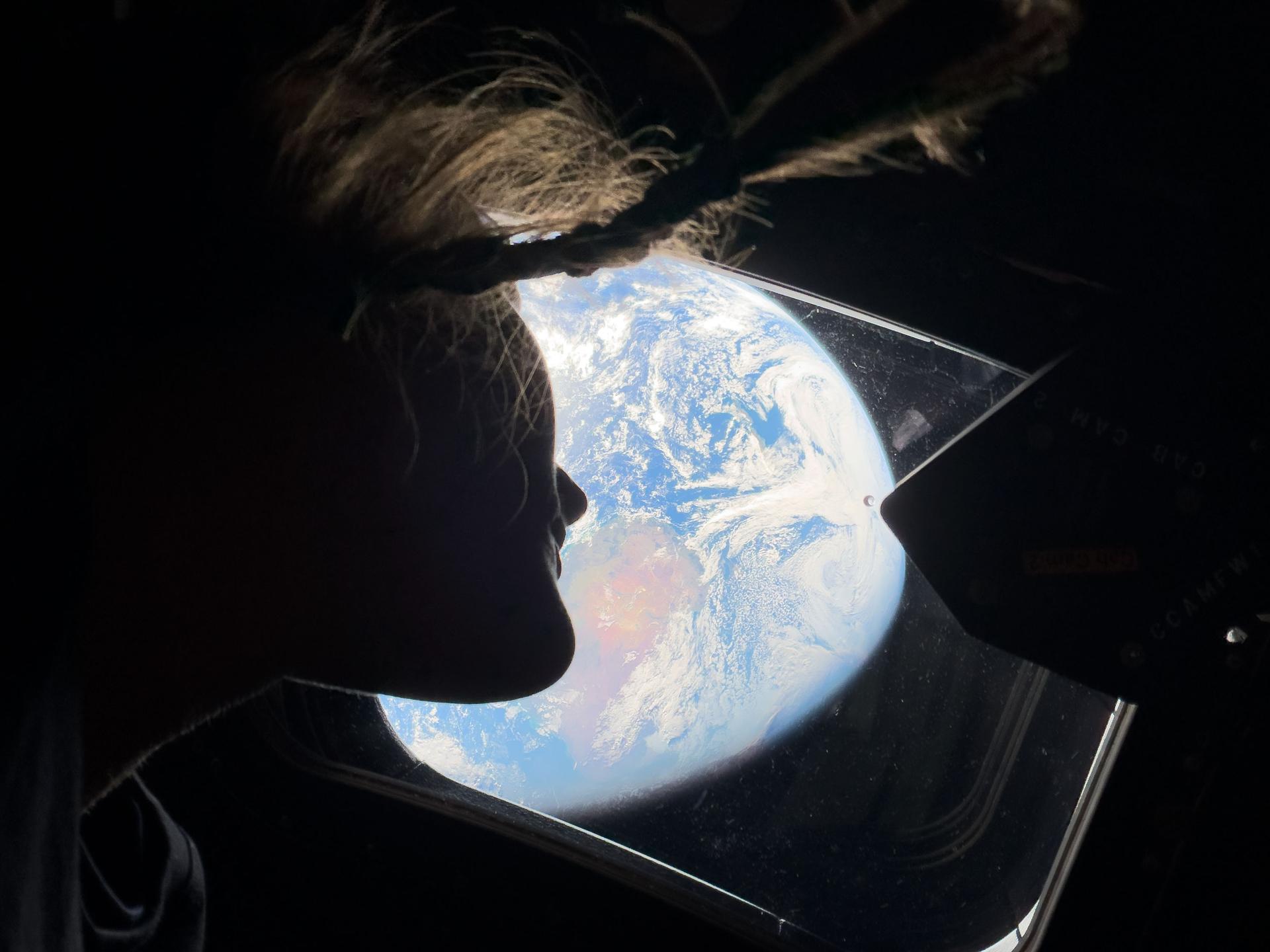 Astronaut Christina Koch peering out an Orion spacecraft window at Earth during Artemis II